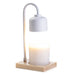 The Polka Dot Press white arched candle warmer lamp with a light wood base and a glowing jar candle on a white background