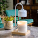 The Polka Dot Press white arched candle warmer lamp with a natural wood base and a glowing jar candle on a table.