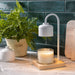 The Polka Dot Press white arched candle warmer lamp with a wooden base and a jar candle on a marble countertop.